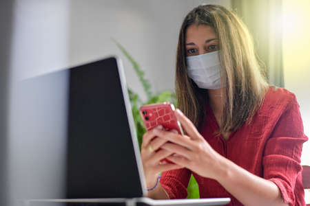 Young female student wearing a protective mask while she is working at home and attending at a...