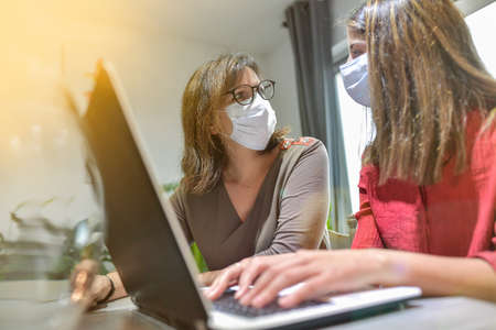 Student and her teacher wearing protective mask and working a lesson on a laptop at home during lockdown due to covid-19の写真素材