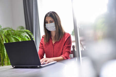 Young female woman wearing a protective mask while she is working at home and attending at a meeting...