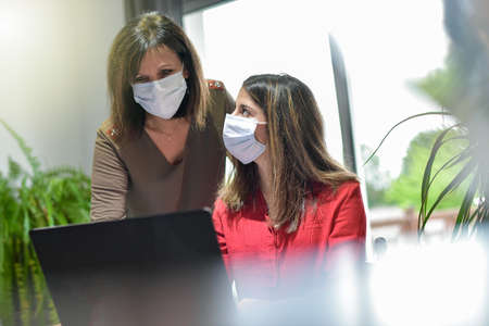 Mother and daughter wearing protective mask and attending online video learning lesson during...