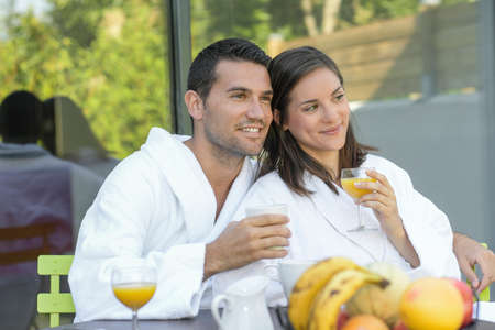 Happy young couple in bathrobes having breakfast outdoorsの写真素材