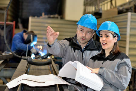 Metal factory manager pointing at something while talking to female apprenticeの写真素材