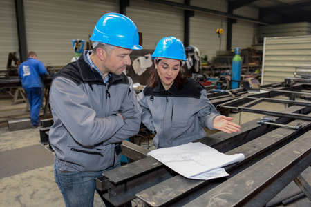 Two workers are looking at the blueprint in a factoryの写真素材