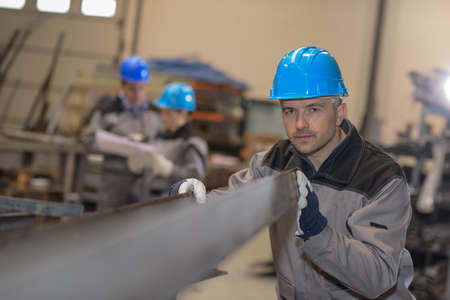 Middle aged male worker positioning a metal bar in metal factoryの写真素材