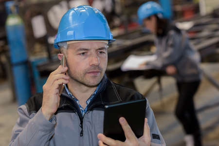 Middle aged male factory eating checks tablets results while talking to someone on the phoneの写真素材
