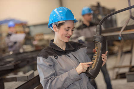 Positive female worker operates heavy machinery in factory