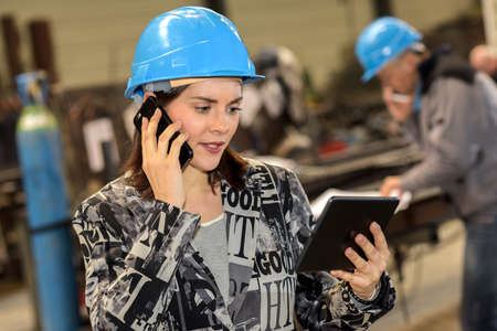 Female metal factory manager on the phone while checking her tabletの写真素材