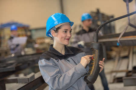 Happy female worker is about to push a button in a metal factoryの写真素材