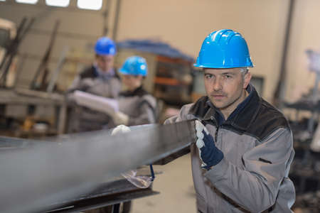 Middle aged male worker positioning a metal bar in metal factoryの写真素材