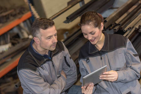 Confident female factory worker shows male colleague something on a tabletの写真素材