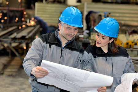 Two workers are looking at some blueprints in the factoryの写真素材