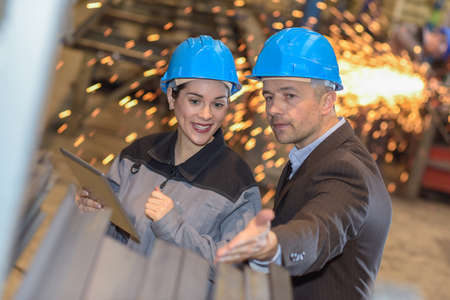 The manager of the factory is showing his female worker how he would like the metal to be finishedの写真素材