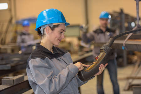 Positive female worker operates heavy machinery in factoryの写真素材