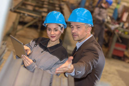 The manager of the factory is pointing at some metal barsの写真素材