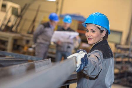 Happy female factory worker moves metal bars in a factoryの写真素材