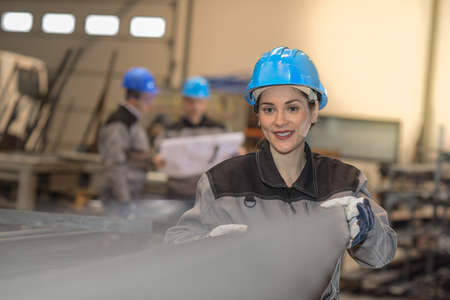 Confident female factory worker moves metal bars in a factoryの写真素材