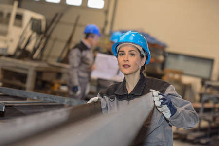 Confident female factory worker moves metal bars in a factoryの写真素材
