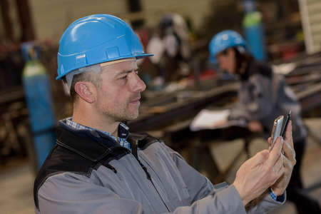 Confused male worker comparing two devices in factoryの写真素材
