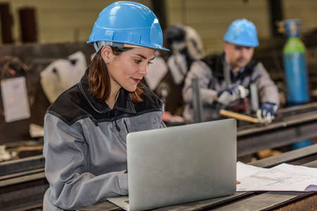 Female engineer works with laptop and blueprints in factoryの写真素材