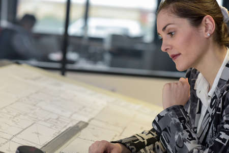 Female architect is looking at blueprint in her officeの写真素材