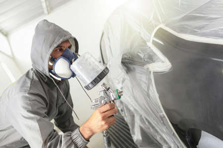 Car body worker paints a car in the paint booth with a spraying paint and a protective maskの写真素材