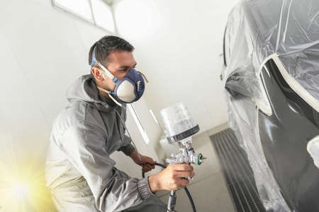 Car body worker paints a car in the paint booth with a spraying paint and a protective maskの写真素材