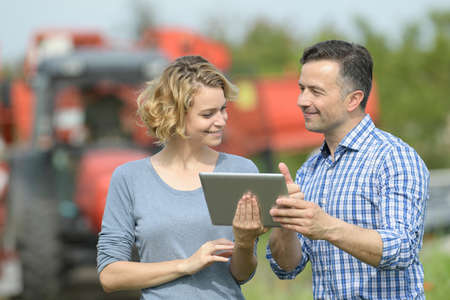 Couple of Farmer analyzes the harvesting data next to the tractor in a fieldの写真素材