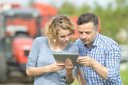 Couple of Farmer analyzes the harvesting data next to the tractorの写真素材