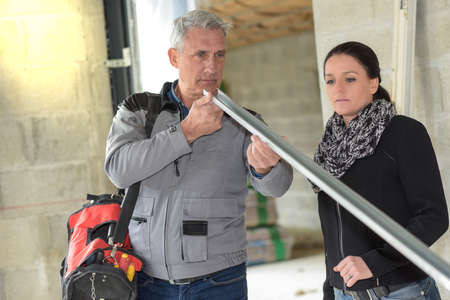 Male worker checks the quality of the materials while his chief inspects the construction siteの写真素材