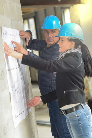 Architect and his assistant are checking a blue-print leaning on the wallの写真素材
