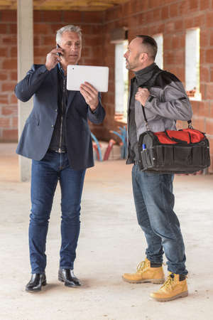 Construction manager and architect read notes in front of a loader backhoeの写真素材