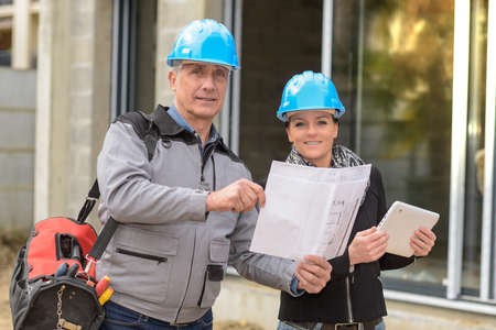 The worker reads the blue-print while the female architect is reading his notes on his tabletの写真素材