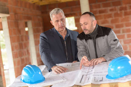 Construction manager and architect read notes in front of a loader backhoeの写真素材
