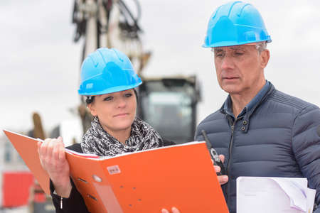 Construction manager and architect read notes in front of a loader backhoeの写真素材
