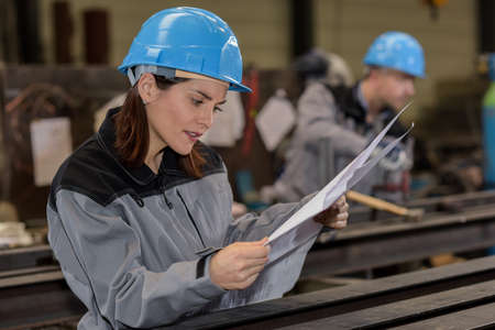 Confused female worker is checking a blueprint in the factoryの写真素材
