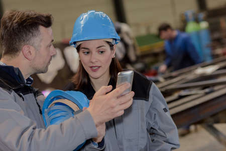 Male worker shows his colleague a mobile-phone in the factoryの写真素材