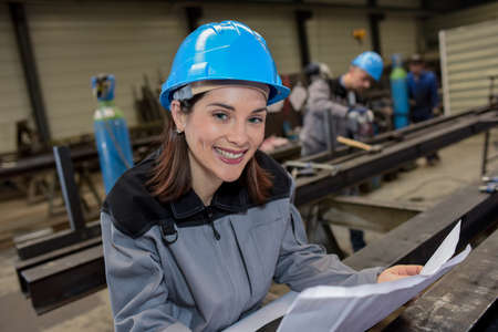 Happy and confident female factory worker reads a blueprint in factory floorの写真素材