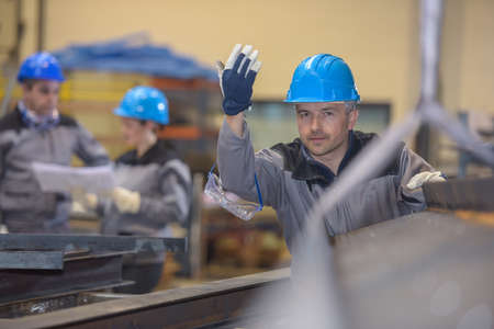 Middle aged factory worker giving a go sign to colleague while shifting a heavy metal barの写真素材