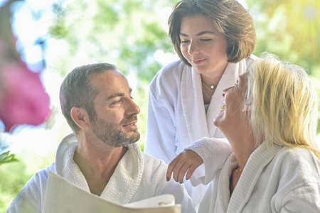 Couple and their daughter wearing bathrobes and having a morning chat on their outdoor patio during breakfastの写真素材