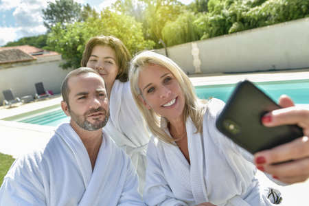 Parents and their daughter in bathrobe having breakfast and and doing selfie outside around their...