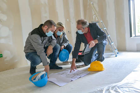 Professional meeting on a construction site between the architect and the craftsmen who wear a protective mask against covid-19の写真素材