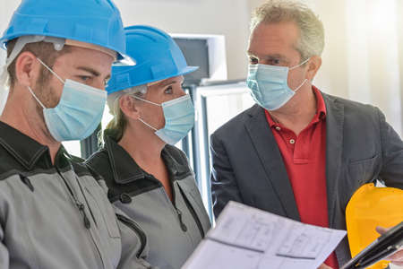 Professional meeting on a construction site between the architect and the craftsmen who wear a protective mask against covid-19の写真素材