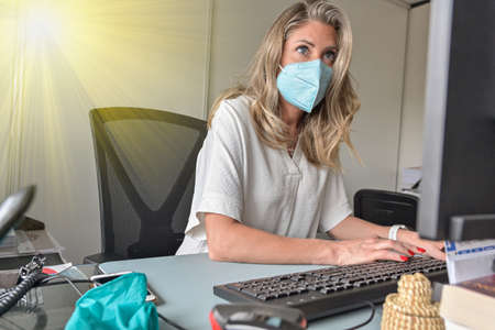 Executive woman working at her desk and wearing a protective mask against covid-19の写真素材