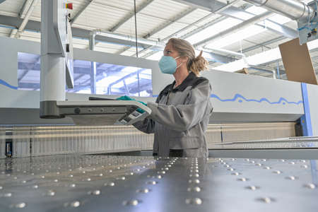 Female engineer is operating on a digital pannel in the company and wearing protections against coronavirusの写真素材