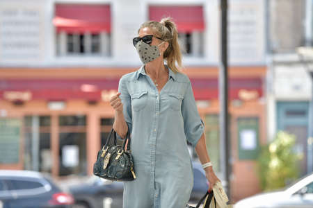 Attractive middle age urban woman walking in the street and carrying bags for shopping while she is wearing a protective mask against corona virus.の写真素材