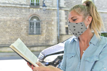 Woman doing a break outdoors during the confinement, reading a book while she is wearing a protective mask against the coronavirusの写真素材