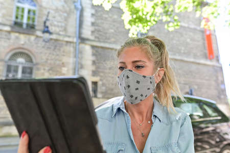 Woman doing a break outdoors during the confinement, reading on her digital tablet while she is wearing a protective mask against the coronavirusの写真素材