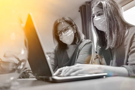 Student and her teacher wearing protective mask and working a lesson on a laptop at home during lockdown due to covid-19の写真素材