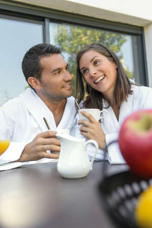 Happy young couple in bathrobes having breakfast outdoorsの写真素材