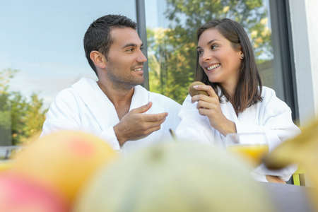 Happy young couple in bathrobes having breakfast outdoorsの写真素材